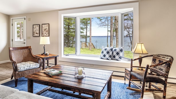 A room with a large window, two rocking chairs, a wooden coffee table, and a blue rug. - Leonards Cabin on Round Lake | Private Dock, 140ft Shoreline, Close to Town - New Rental (Hayward)