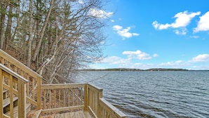 A wooden deck with steps leading to a lake, surrounded by trees and a clear sky. - Leonards Cabin on Round Lake | Private Dock, 140ft Shoreline, Close to Town - New Rental (Hayward)