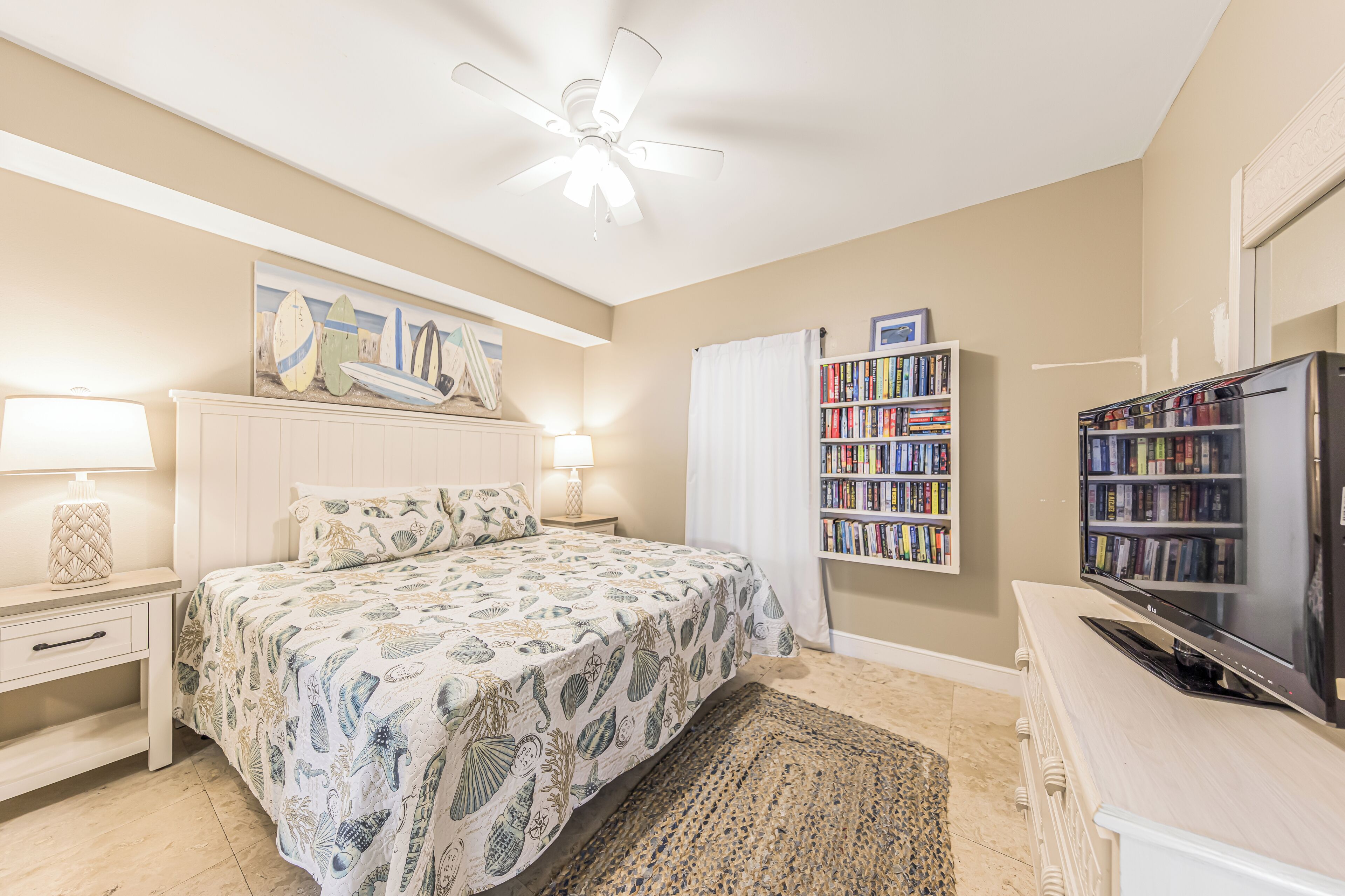 Una camera da letto con un letto, una ventola a soffitto, una libreria, una televisione e un comodino.