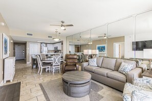 A spacious living room with a sofa, armchair, and ottoman, a dining area with chairs, and a kitchen in the background. - Breathtaking Views in this 3 BR 2 BA in Tower 1 at the Majestic!!!! (Panama City Beach)
