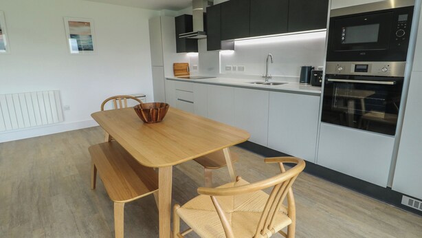 Una cocina moderna con una mesa de madera, dos sillas, un microondas y un horno empotrado.