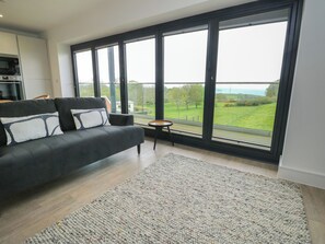 A modern living room with a large window, a sofa, and a small side table. - Glynllifon 5 (Marianglas)