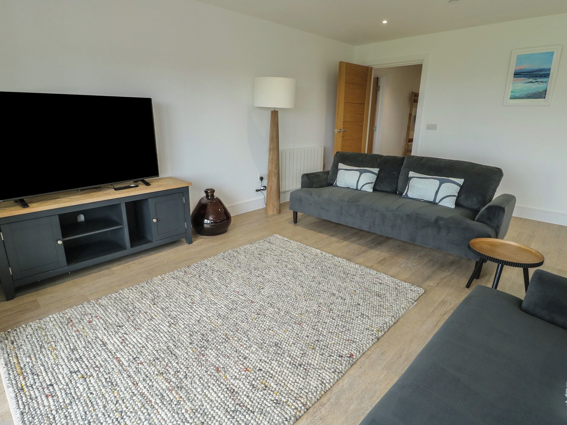 A living room with a flat-screen TV, grey sofa, dark wooden entertainment unit, and a patterned rug.