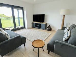 A modern living room with a TV, sofa, and a small wooden table. - Glynllifon 5 (Marianglas)