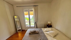 Un dormitorio con cama, mesita de noche con lámpara, ventana con cortinas y vistas al exterior.
