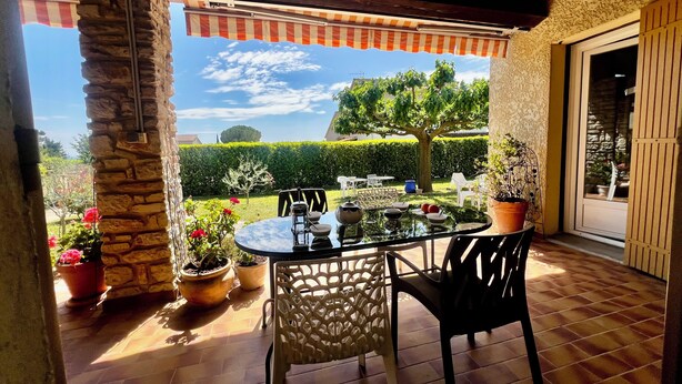 Un patio con una mesa y sillas, plantas en macetas y vista a un jardín.