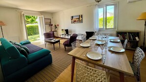 Una sala de estar con un sofá, una mesa de comedor preparada para cuatro, un televisor y una estantería.