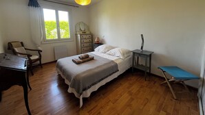Un dormitorio con cama, una silla, un escritorio, un aparador, una mesita de noche y una ventana.