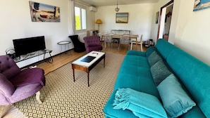 Una sala de estar con sofá, sillas, televisor, mesa de comedor y obras de arte en las paredes.