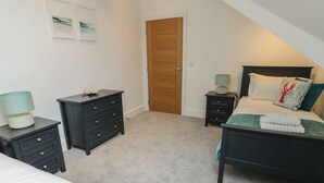 A bedroom with a bed, a dresser, a nightstand, and a door. - Glynllifon 7 (Marianglas)