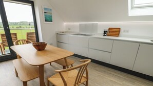 A modern kitchen with white cabinets, a wooden dining table, and chairs. - Glynllifon 7 (Marianglas)
