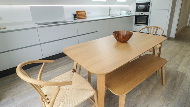 A modern kitchen with a wooden table, two chairs, and a bowl on the table. - Glynllifon 7 (Marianglas)