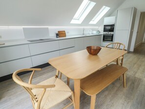 A modern kitchen with a wooden table, two chairs, and a bowl on the table. - Glynllifon 7 (Marianglas)