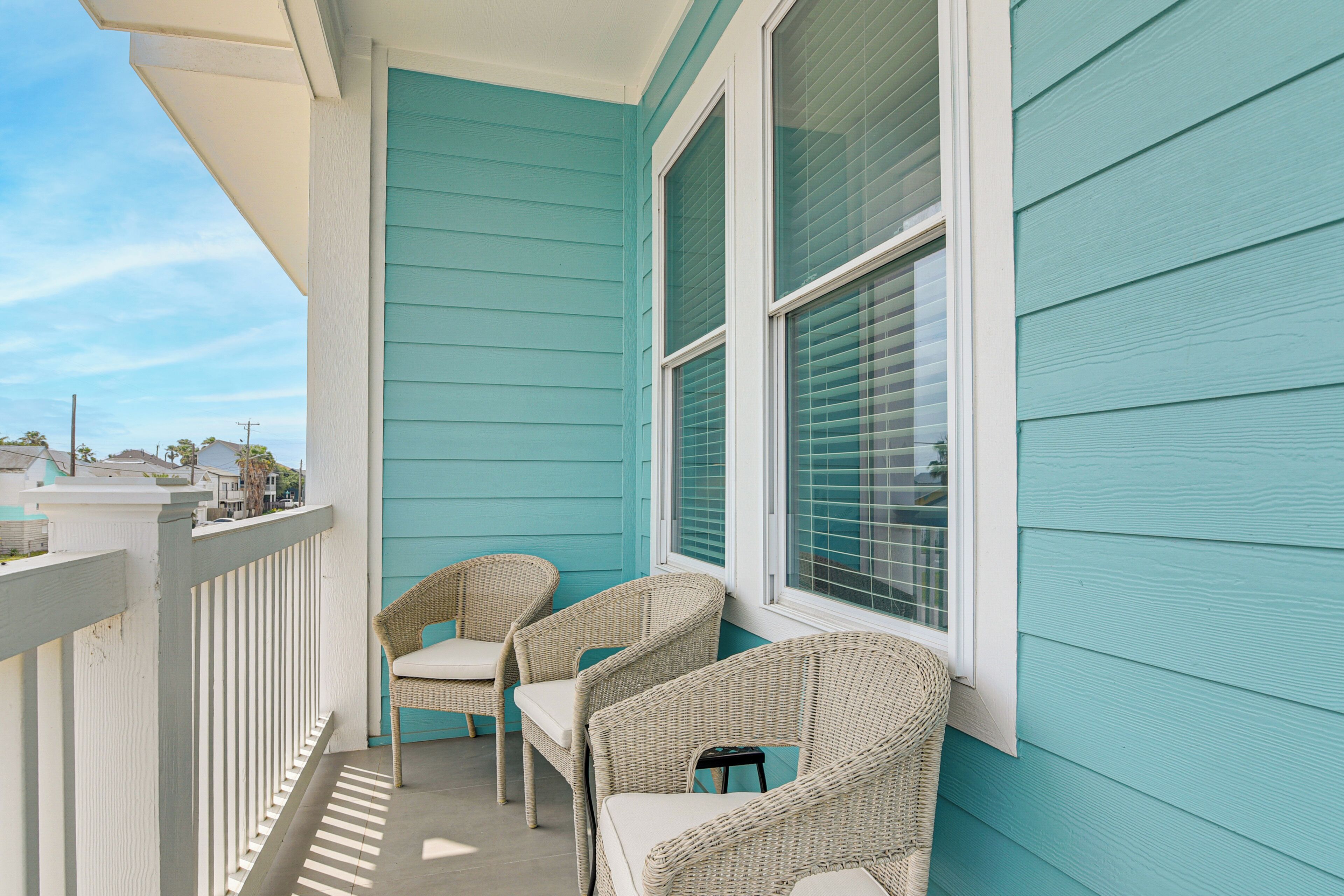 Een balkon met rieten stoelen en een witte reling.