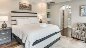 Ein Schlafzimmer mit einem großen Bett, Nachttischlampen, einem Nachttisch, einem Sessel und einem Gemälde an der Wand.