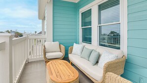 Ein Balkon mit weißer Brüstung, einem Korbsessel mit Kissen und einem Holztisch.