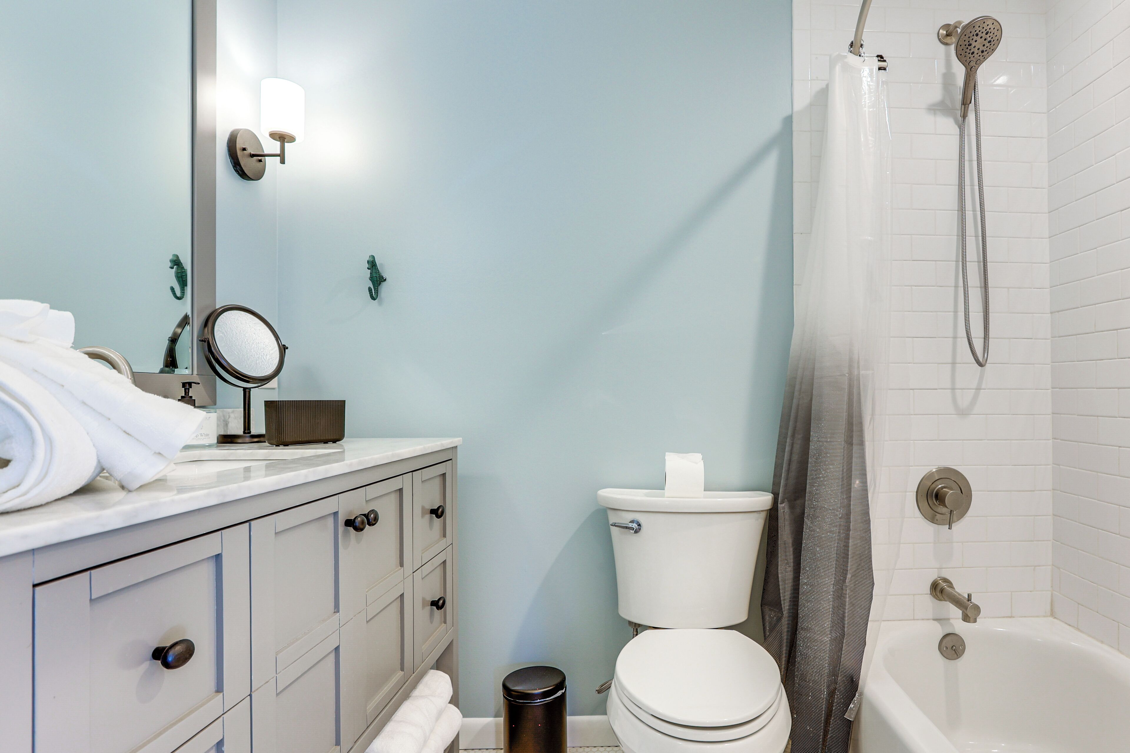 Un baño con inodoro, lavamanos con espejo, toallero y ducha.