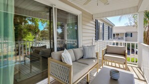 A covered porch with a sofa, a chair, and a table with dishes. - Pool Access! St Simons Island Getaway w/ Balcony (St. Simons Island)