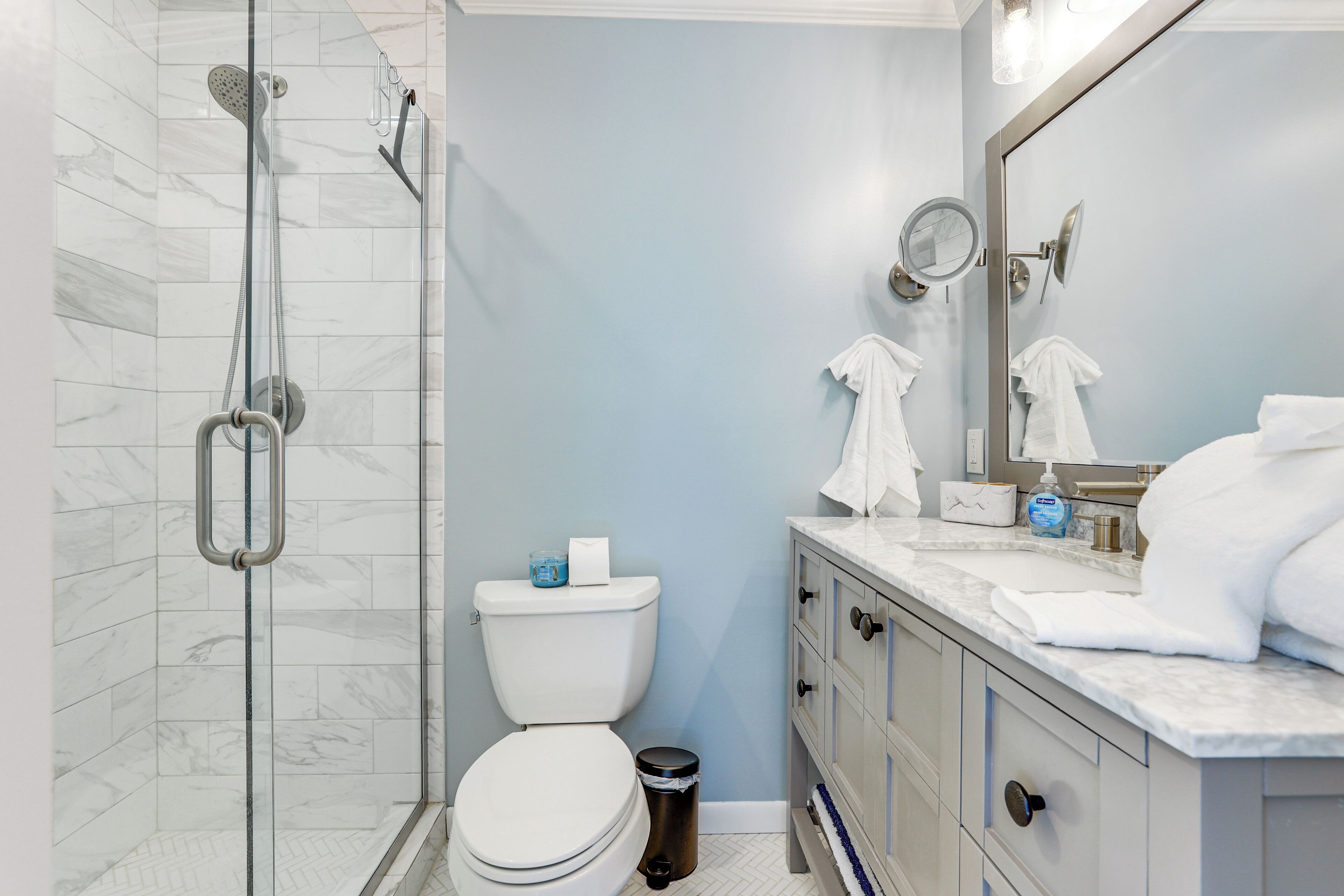 Un baño con ducha envuelta en vidrio, inodoro, lavabo con espejo y cubo de basura.