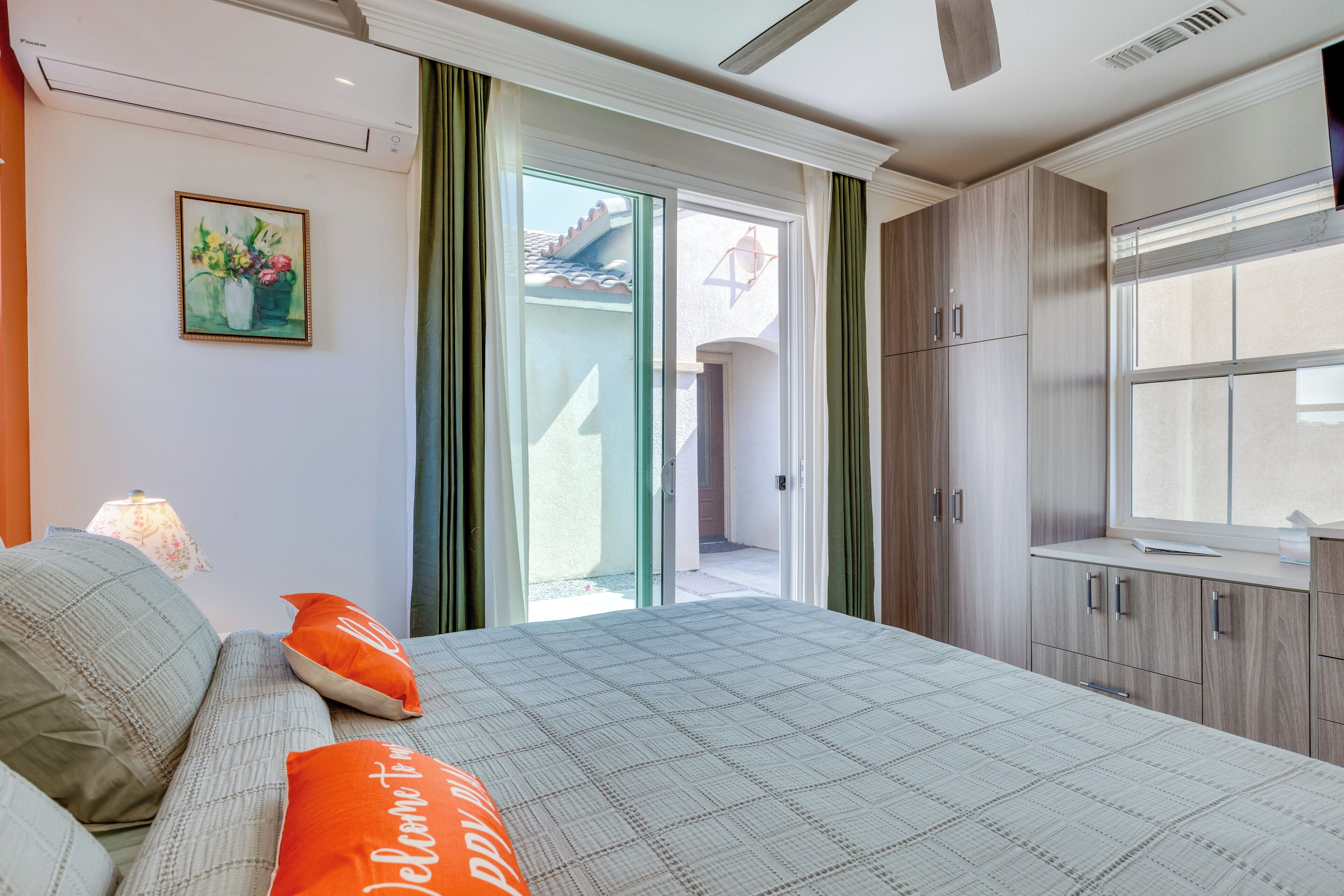 Un dormitorio con cama, almohadas, una mesita de noche, una ventana y una puerta que da a un espacio exterior.