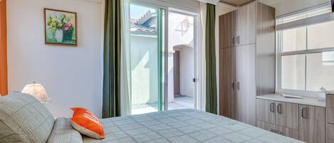 Un dormitorio con cama, almohadas, una mesita de noche, una ventana y una puerta que da a un espacio exterior.