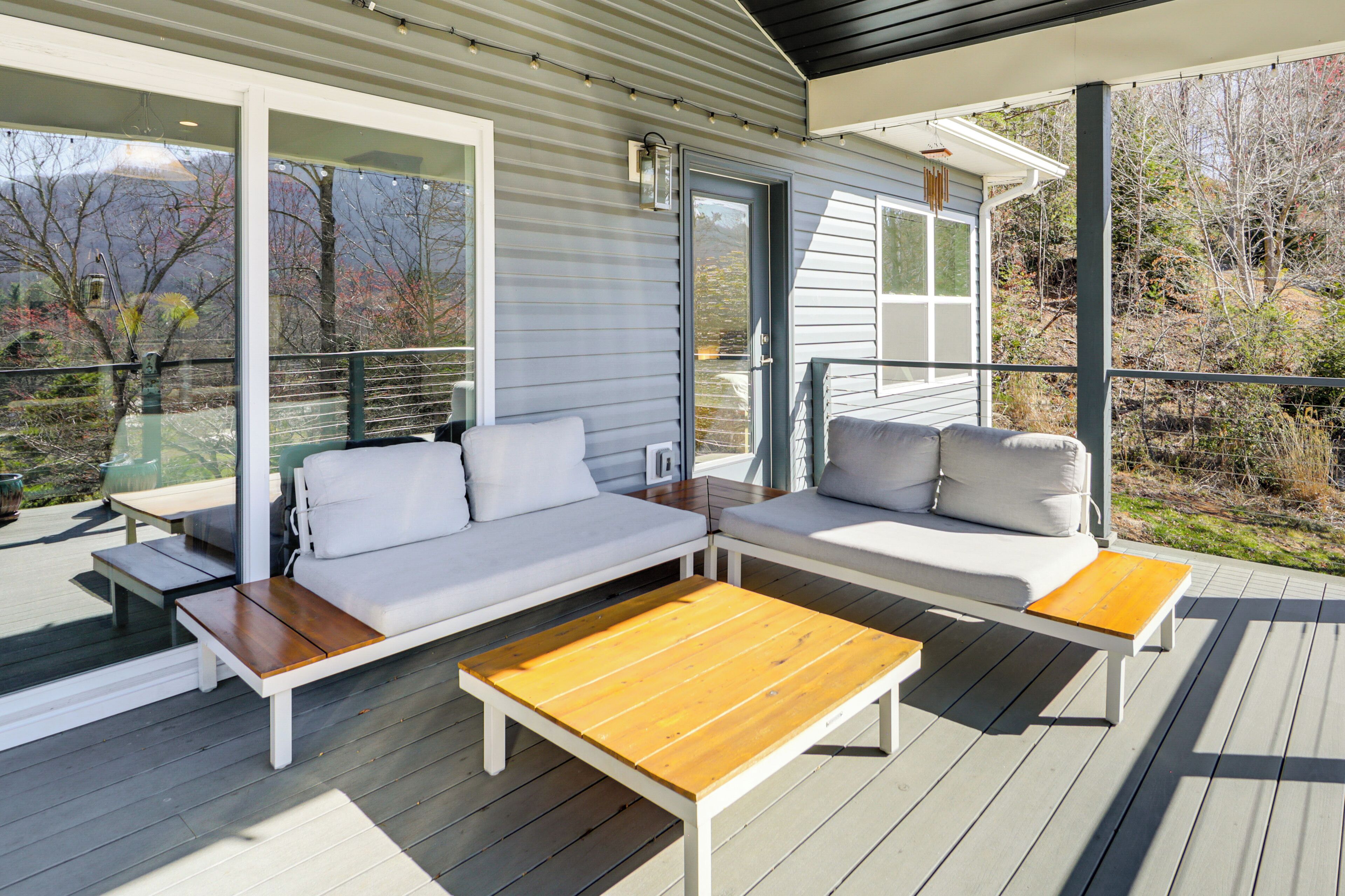 A deck with a sofa, two wooden tables, and a view of the surrounding landscape.