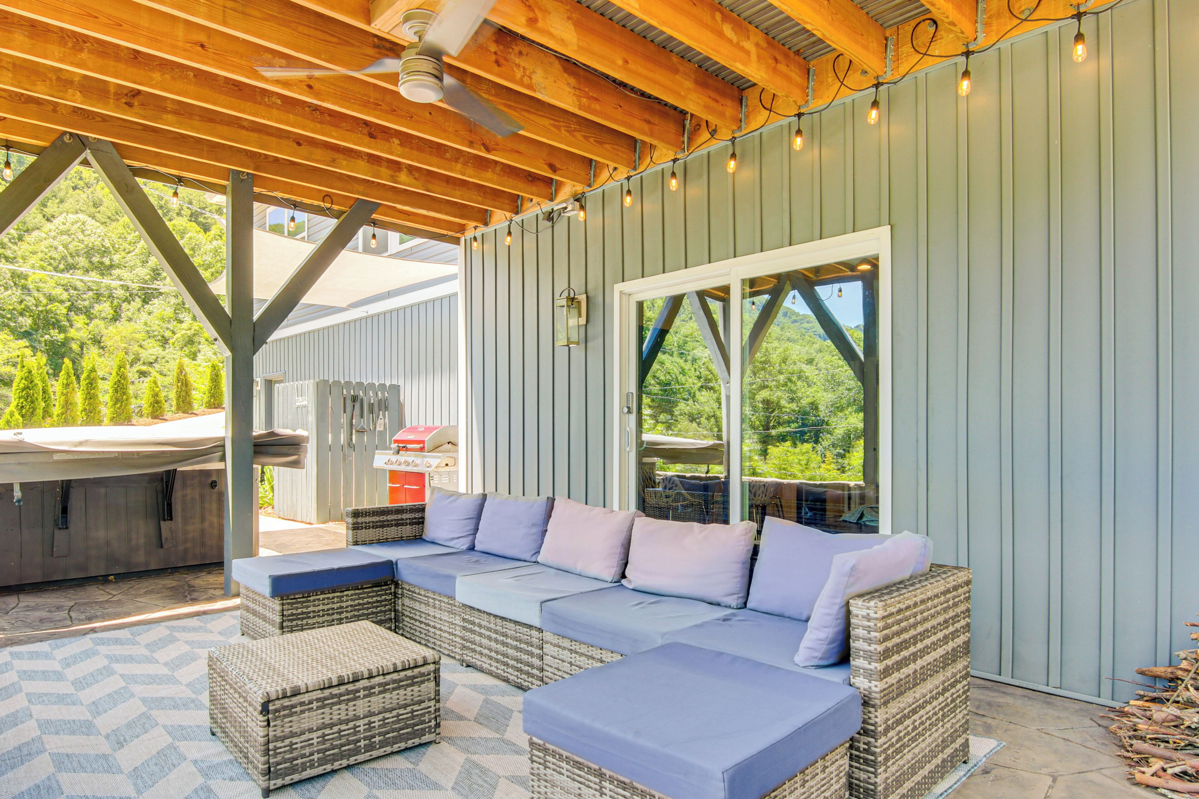 A covered outdoor seating area with a sofa, wicker furniture, and a hot tub.