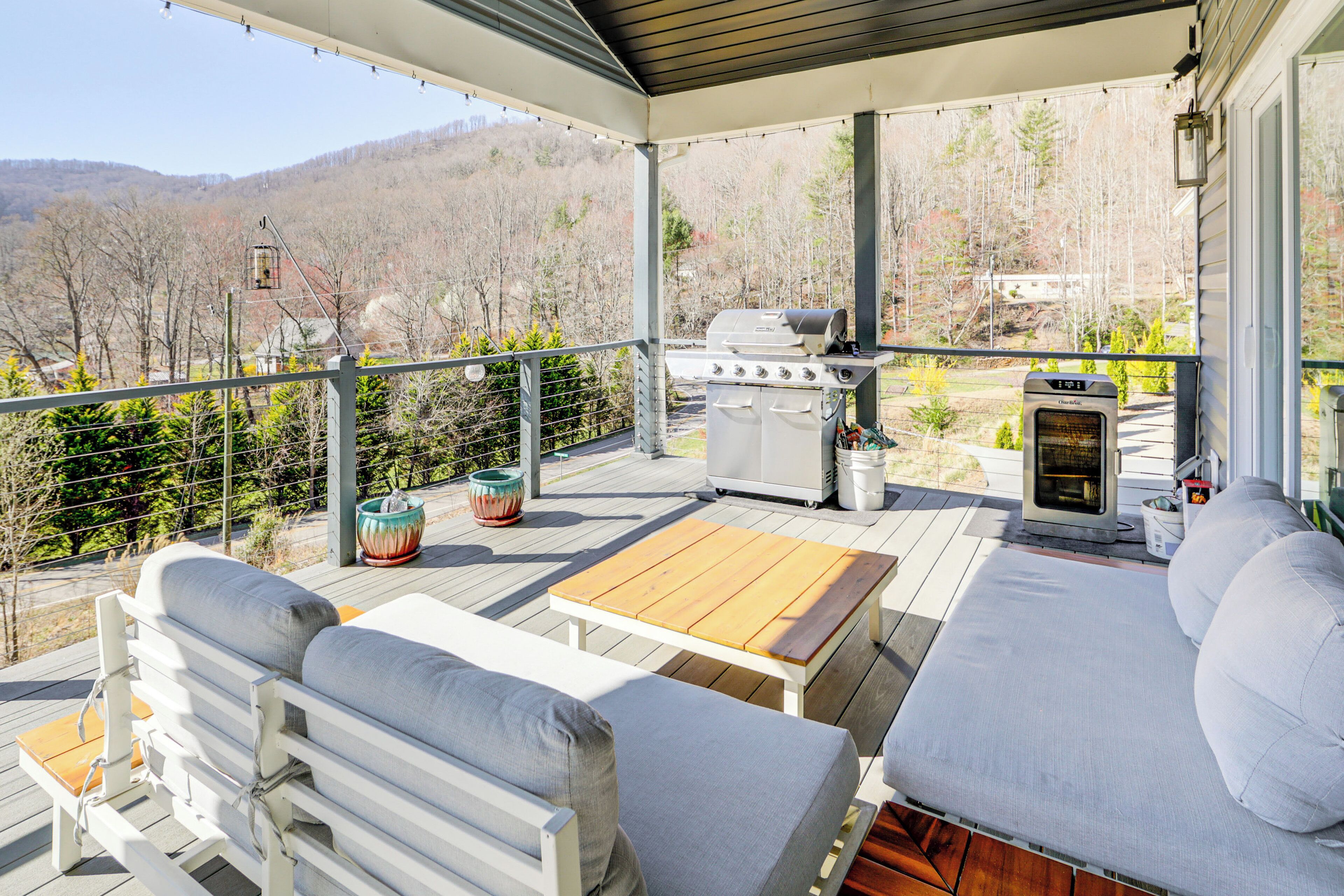 Una terraza cubierta con una parrilla, asientos y vistas a las montañas.