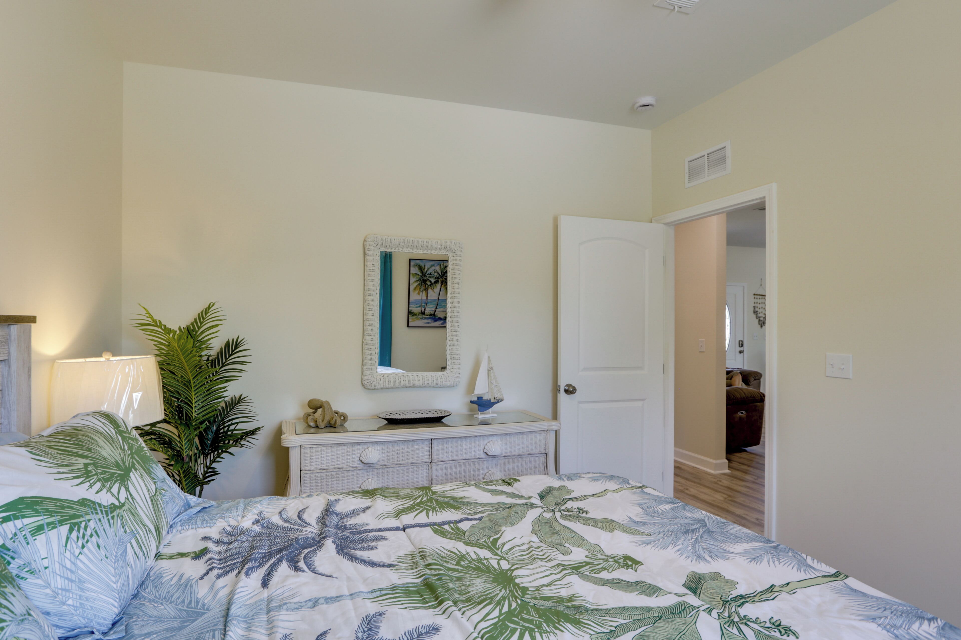 Une chambre à coucher comprenant un lit, une commode, un miroir, une plante et une porte donnant sur une autre pièce.
