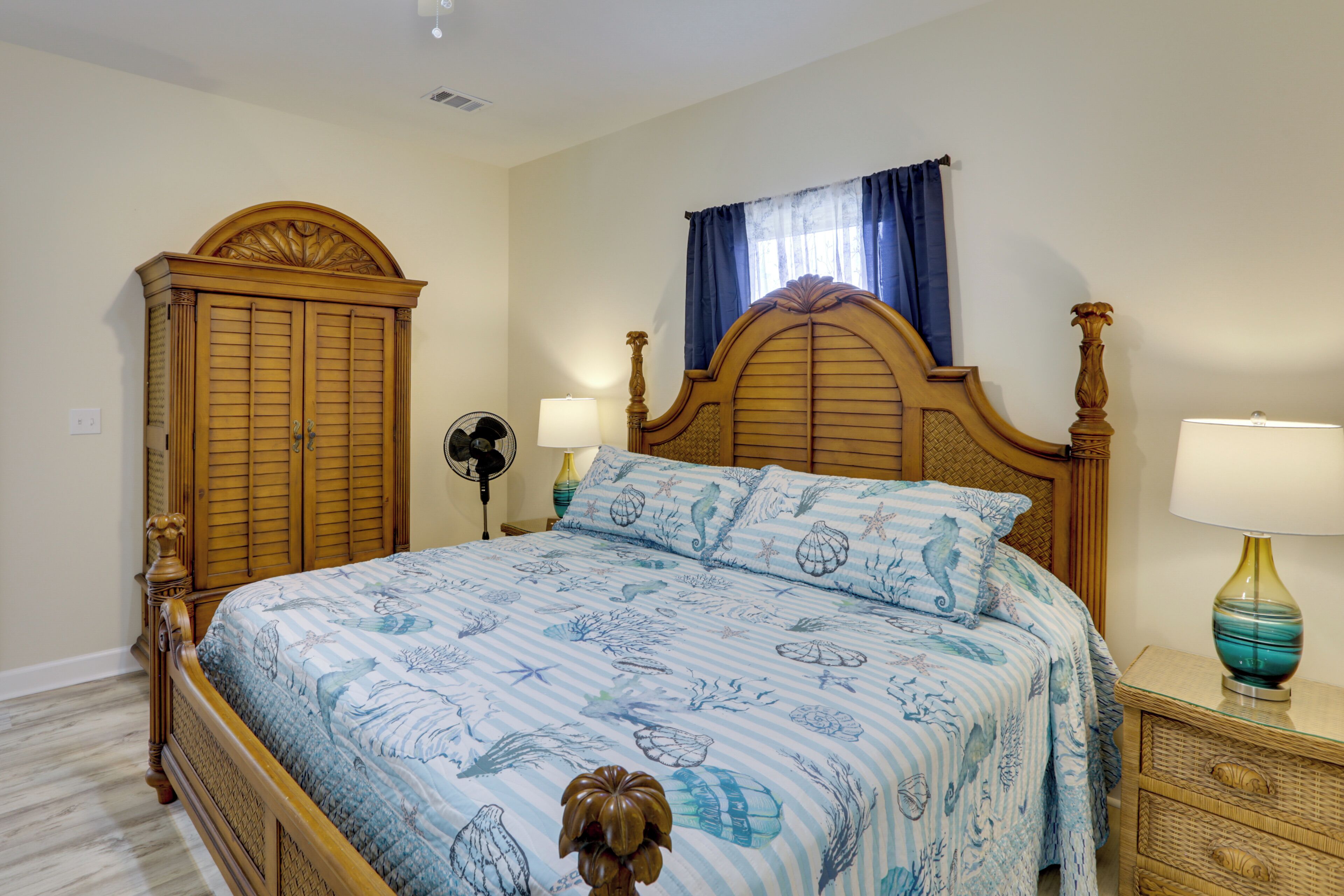 Un dormitorio con una cama de madera, una mesita de noche con lámpara, un aparador y una ventana con cortinas.