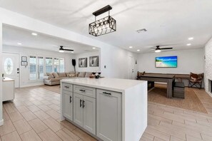 A spacious living area with a large island, a dining table, and a view of the outdoors.