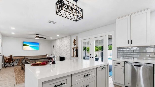 A modern kitchen with white cabinetry, a central island, stainless steel appliances, and a ceiling fan. - Sunrise-Sparkling Pool-BBQ Grill-Mins to Old Town (Scottsdale)