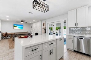 Une cuisine moderne avec des meubles blancs, un îlot central, des appareils en acier inoxydable et un ventilateur de plafond.