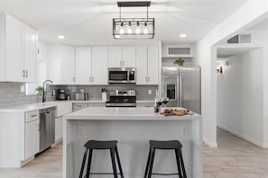 Een moderne keuken met witte kasten, roestvrijstalen apparatuur, een centraal eiland met barkrukken en een hangende lamp.
