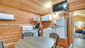 Una cocina compacta con paredes de madera, una mesa redonda para comer y servicios básicos, incluyendo microondas, estufa y refrigerador.