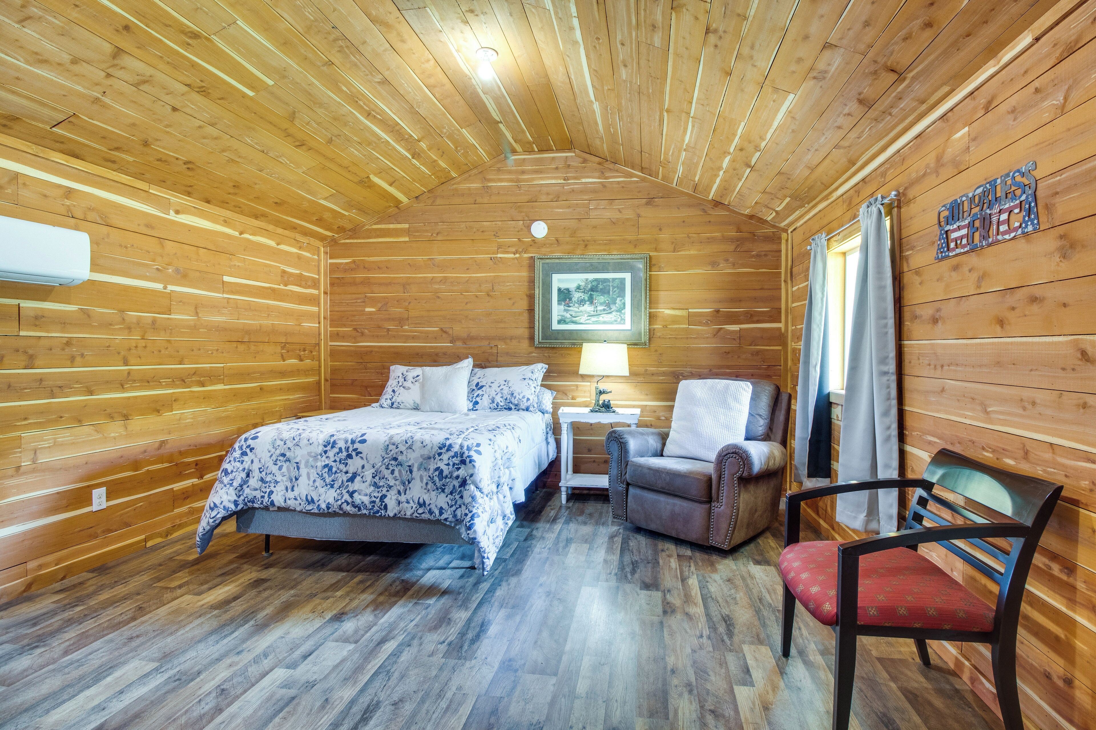 A wooden cabin room with a bed, a chair, a nightstand, and a lamp.