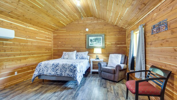 Una habitación de cabaña de madera con una cama, una silla, una mesita de noche y una lámpara.
