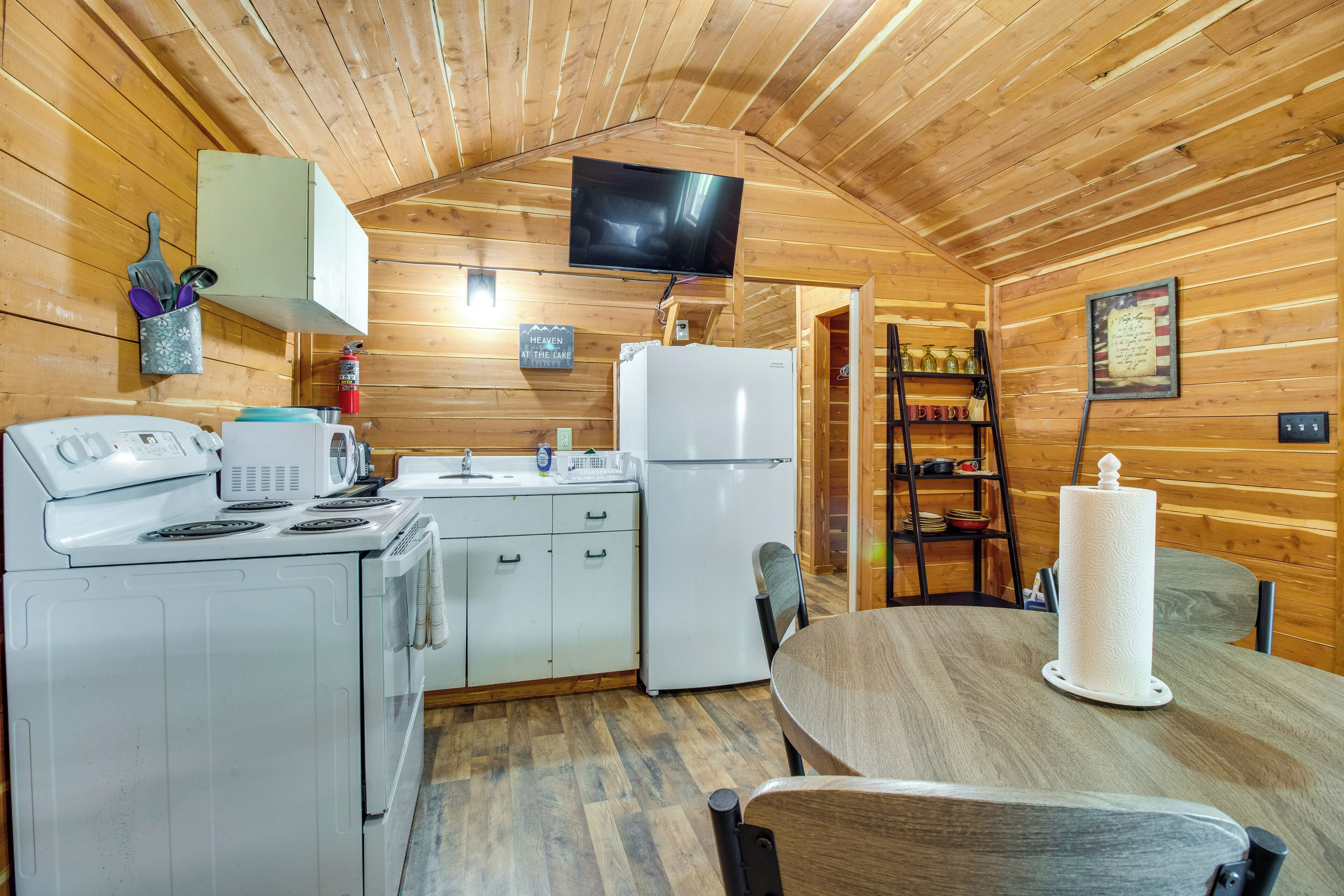 A wooden cabin interior with a kitchen, a dining table, a television, and a sign on the wall.
