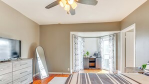 Un dormitorio con cama, televisor, ventilador de techo y vistas a un balcón.