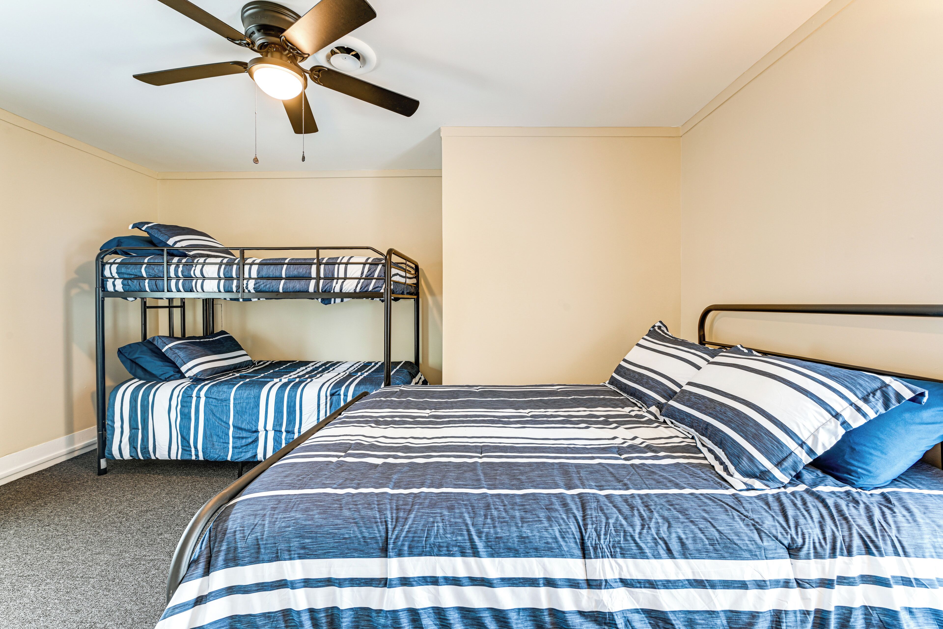 A room with bunk beds, a ceiling fan, and a carpeted floor.