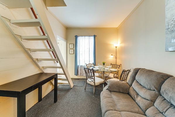 Un salon confortable avec un canapé, une table à manger et des chaises, un escalier et une fenêtre avec des rideaux.