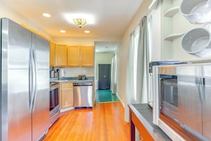 A compact kitchen with stainless steel appliances, wooden cabinets, and a green floor.