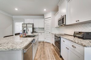 Une cuisine moderne avec des meubles blancs, des comptoirs en granit, des appareils en acier inoxydable et un dosseret de carrelage disposé en motif chevron.