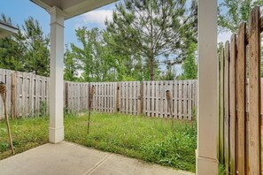 A covered patio area with a wooden fence, concrete flooring, and surrounding greenery.