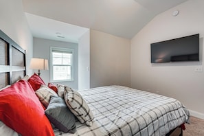 A bedroom with a bed, pillows, a TV, a window, and a door.