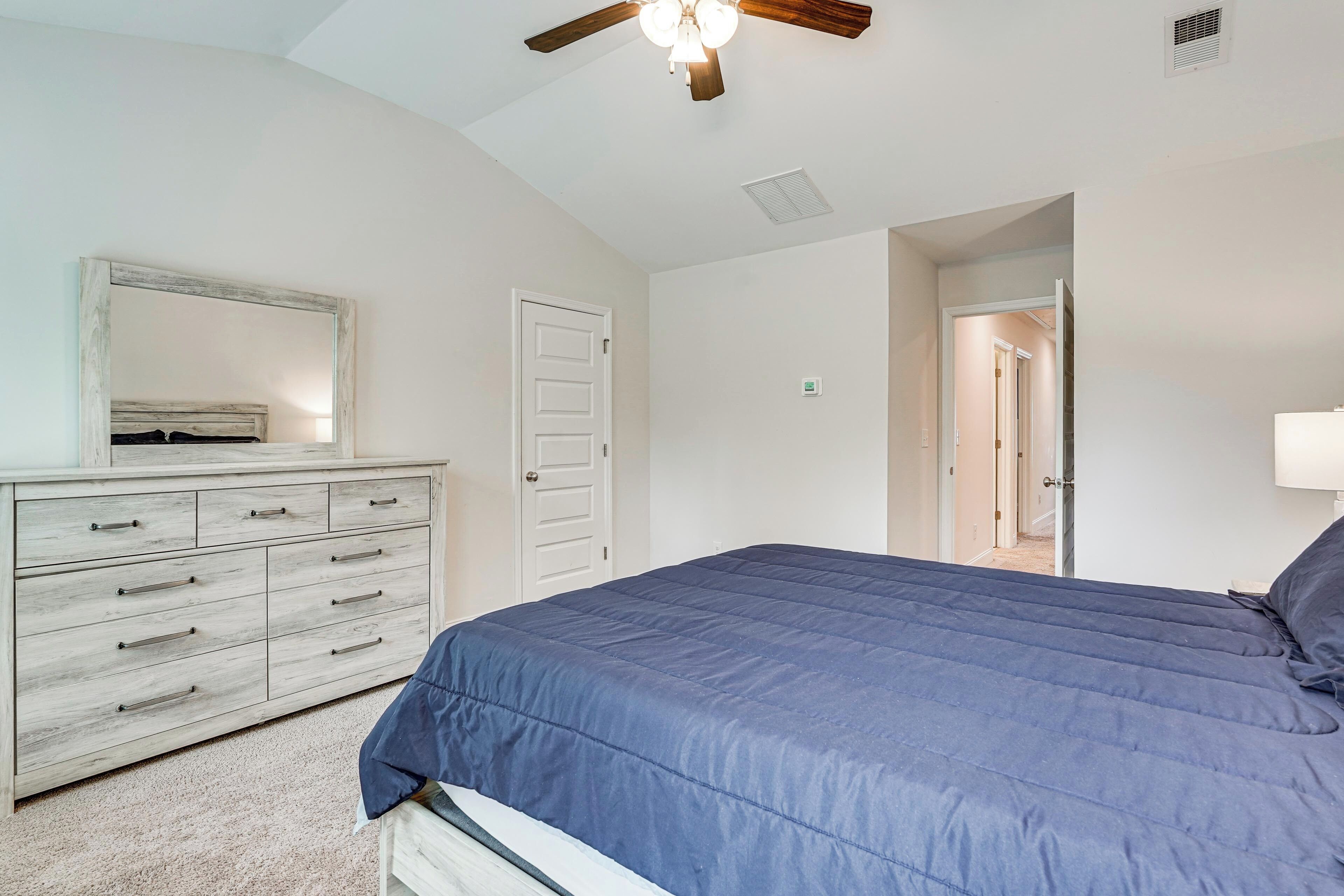 A bedroom with a bed, a dresser, a ceiling fan, and a door leading to another room.