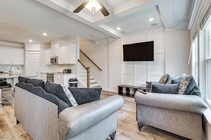 A modern living room with a sofa, armchairs, a TV, and a kitchen in the background. - Easy Access to Golf Club & Dtwn: Augusta Basecamp (Evans)