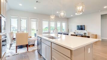 A modern kitchen with a large island, stainless steel appliances, and pendant lighting.