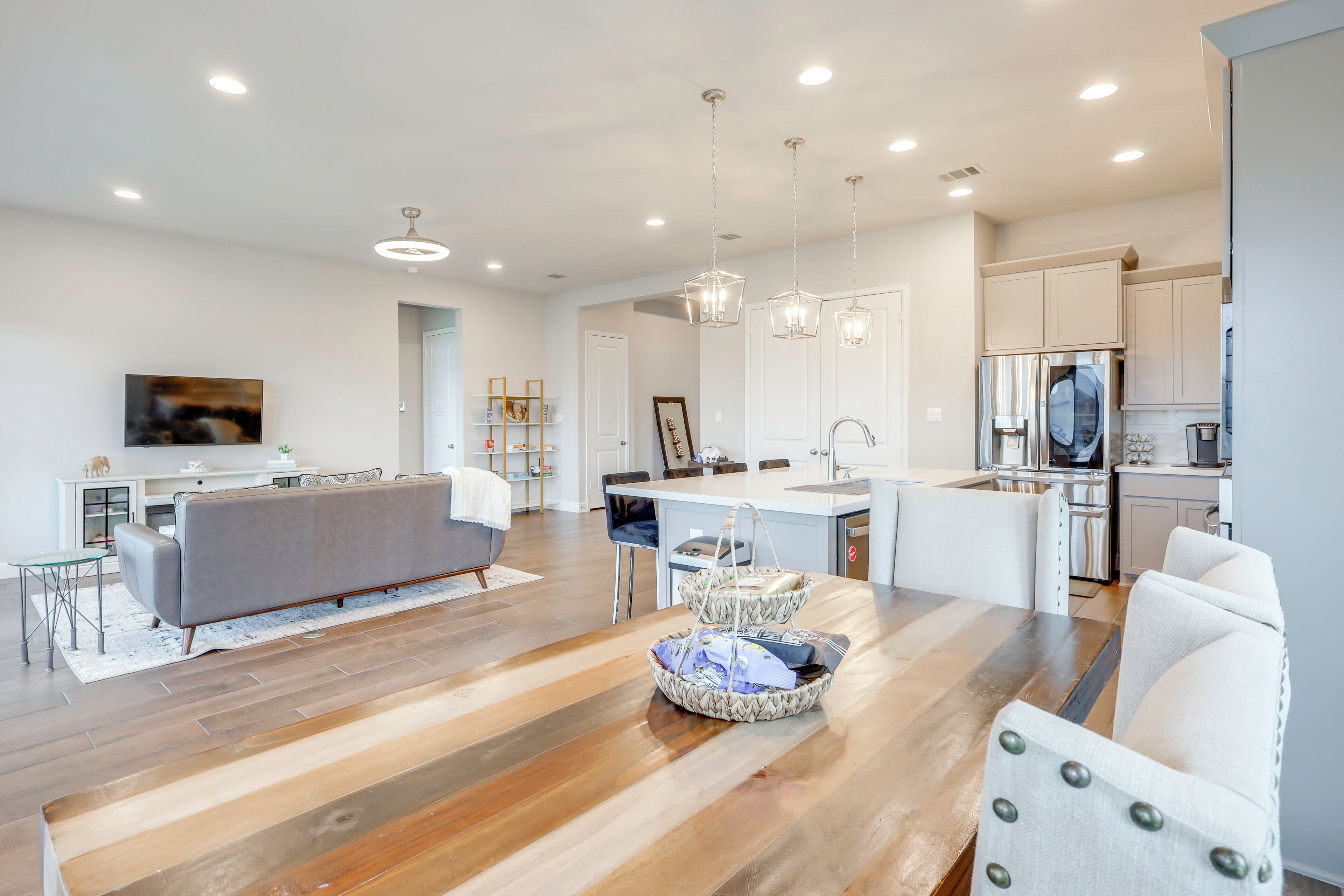 A modern kitchen with white cabinets, a stainless steel refrigerator, and a dining area with a wooden table and white chairs.