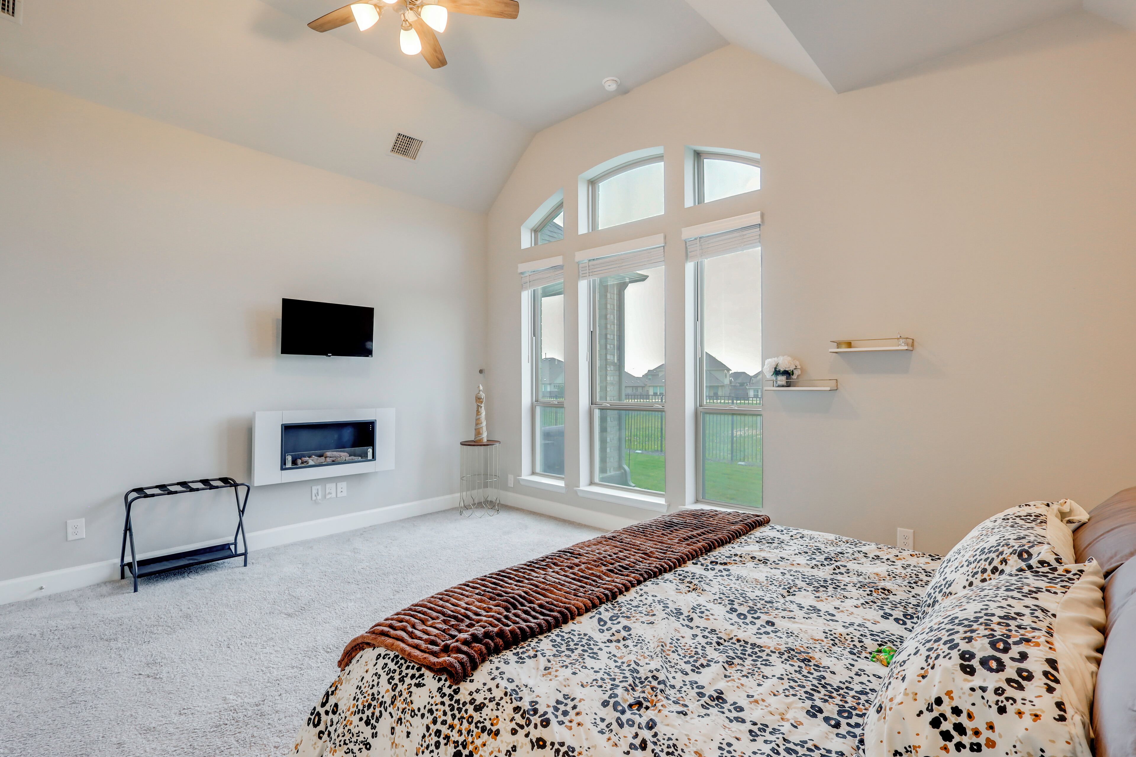 A bedroom with a large bed, a television mounted on the wall, a window with a view of the outside, and a ceiling fan.